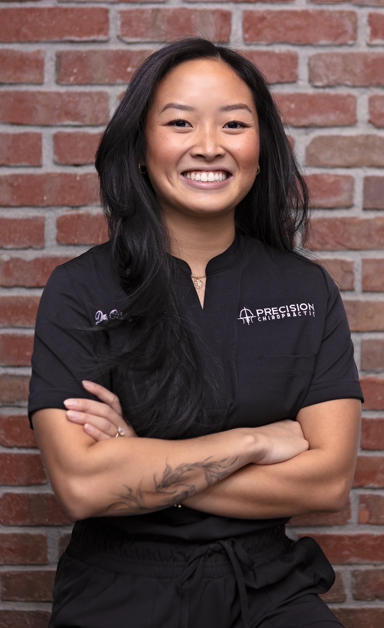 Dr. Olivia La standing with arms crossed in Precision Chiropractic scrubs, strategic partner of the Combat Recovery Foundation